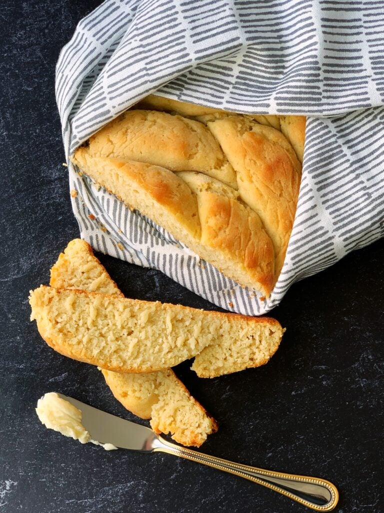a loaf of gluten free plait bread wrapped in fabric with a few individual slices beside it