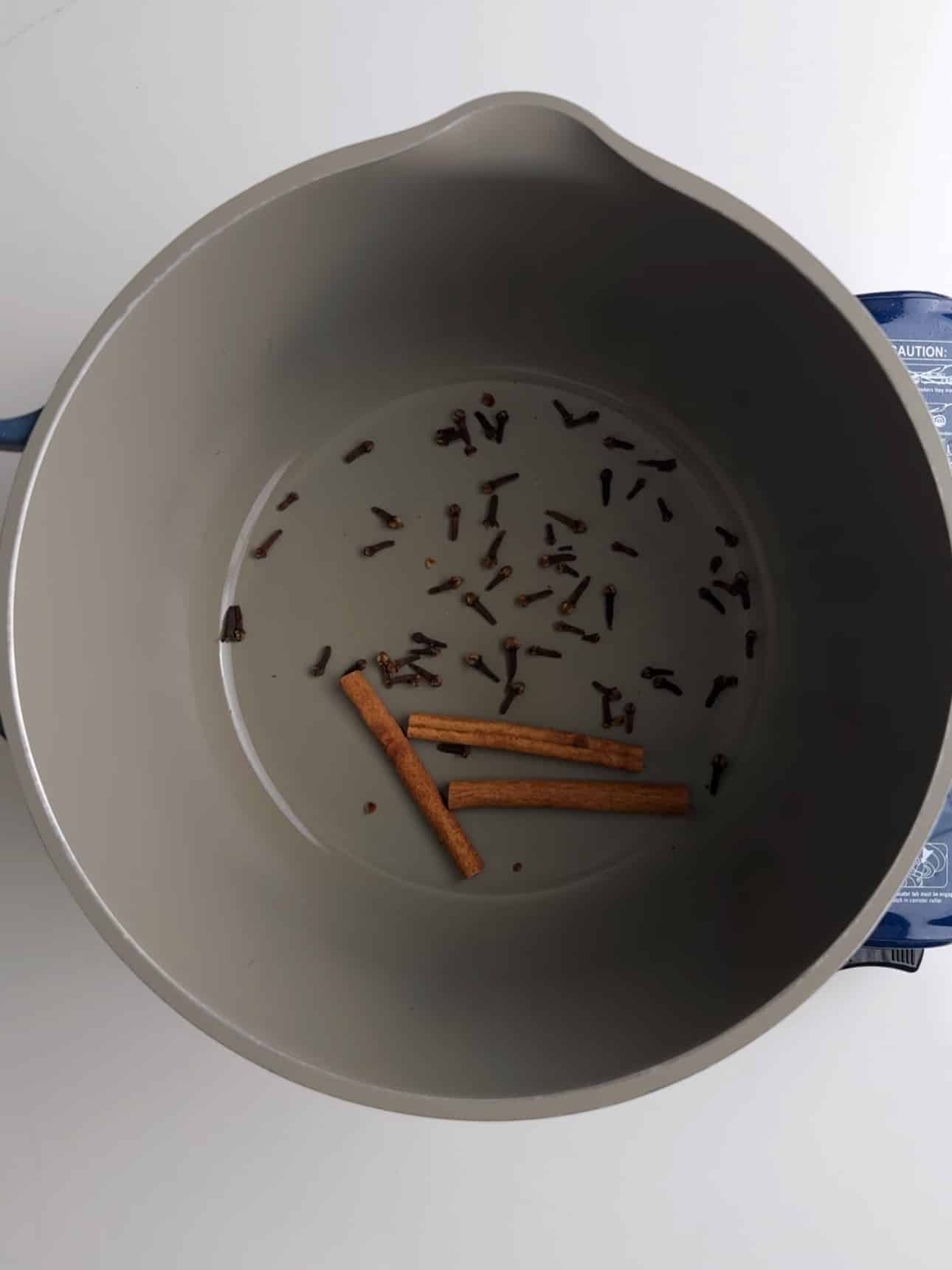 Cloves and cinnamon warming up in a grey pot.