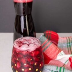 Glass filled with sorrel and ice cubes. A carafe of sorrel is in the background.