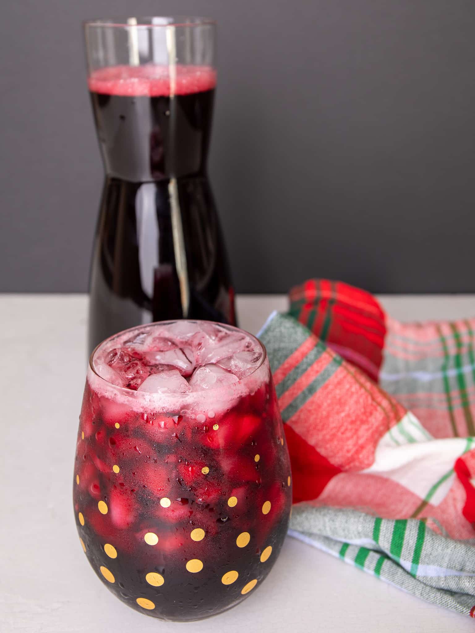 Glass filled with sorrel and ice cubes. A carafe of sorrel is in the background.