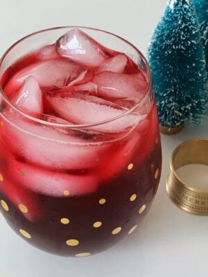 Glass filled with sorrel and ice cubes with tiny christmas trees and napkin rings that say Merry