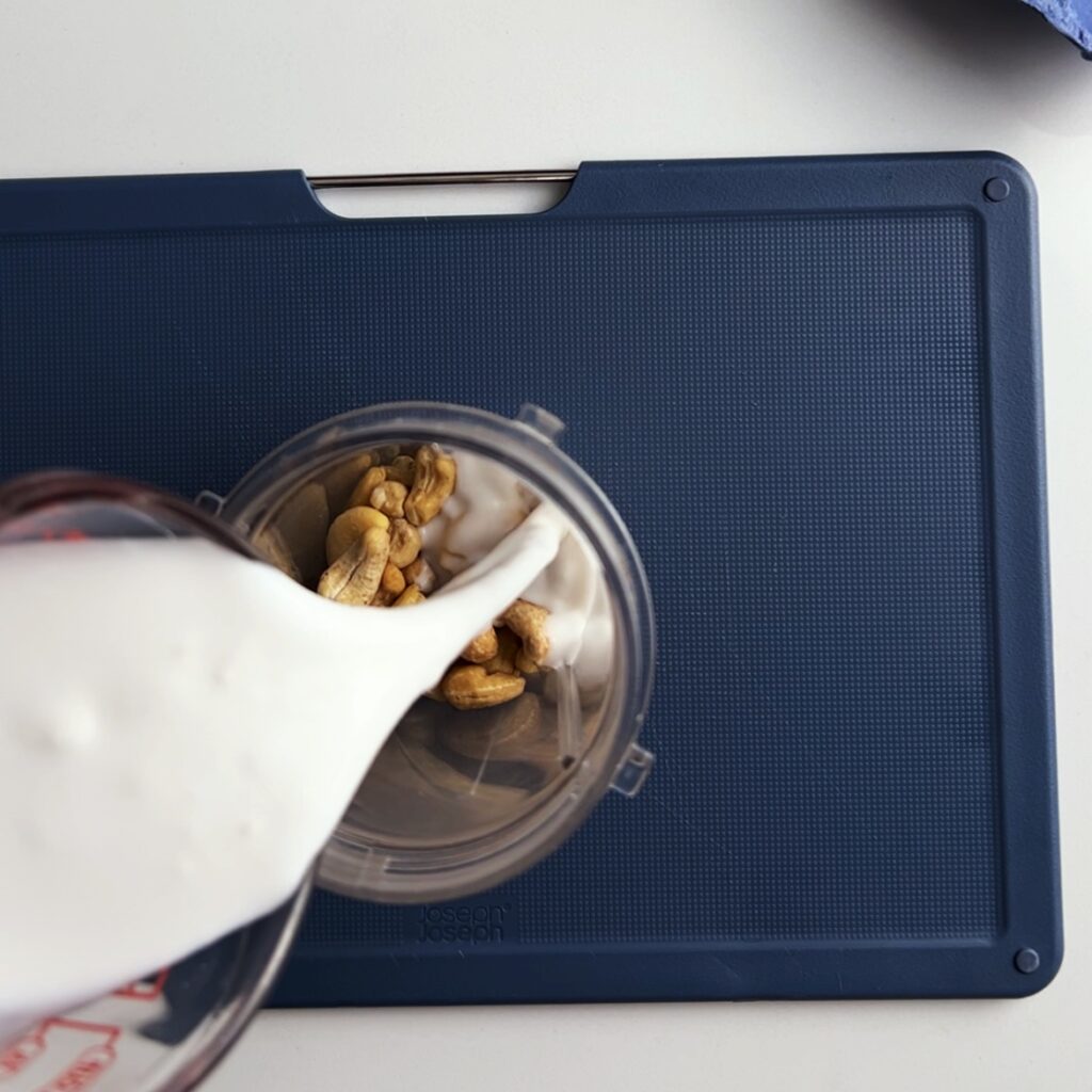 pouring coconut milk into the cashew cream ingredients in a blender cup