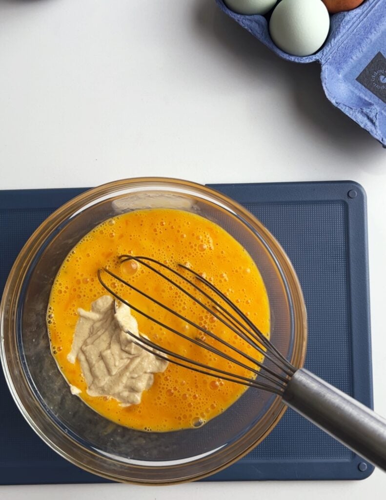 cashew cream with whisked eggs in a bowl, with the whisk sitting in the mixture