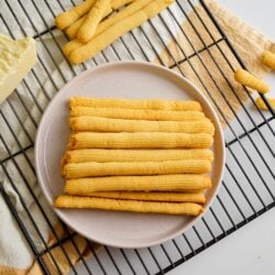 Cheese straws stacked in a plate on cooling rack with a cream and orange towel under the cooling rack