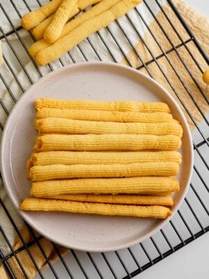 Cheese straws stacked in a plate on cooling rack with a cream and orange towel under the cooling rack