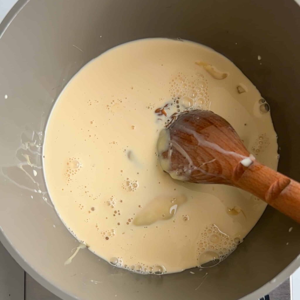 Milk in a pot with a brown wooden spoon.