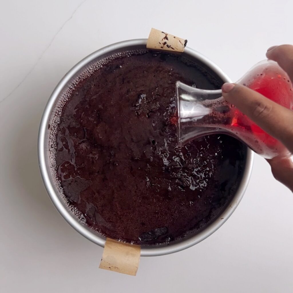 a hand pouring sparkling grape juice over freshly baled black cake