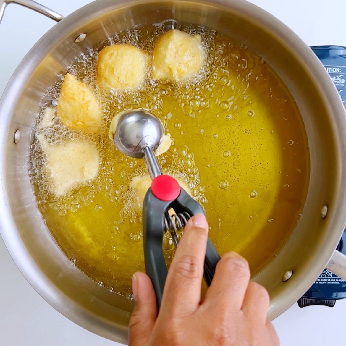 A brown hand dropping malasadas (guyanese pancakes) in hot oil