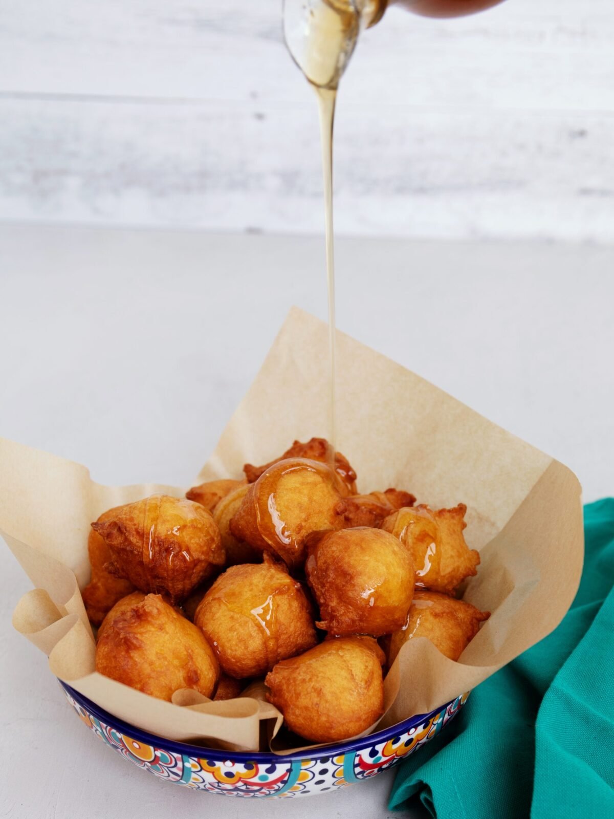 Malasadas featured in a bowl and pouring syrup