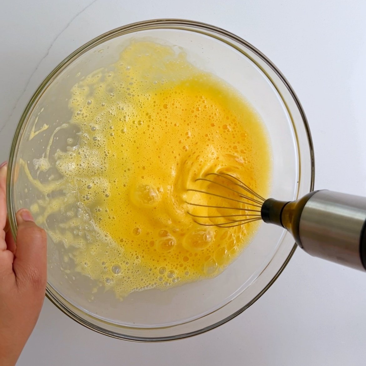 Whisking eggs in a glass bowl with an electric whisk