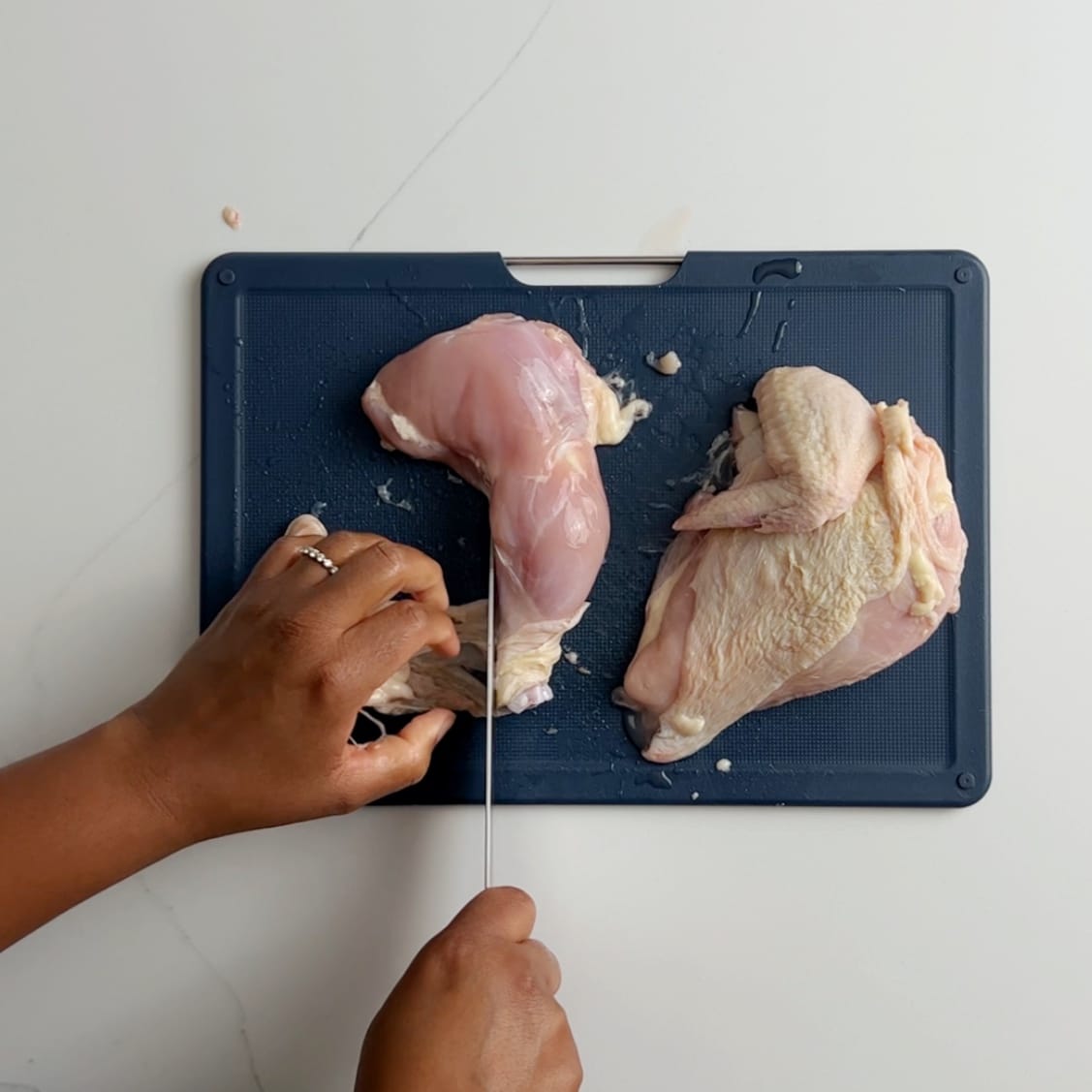 Removing the skin from chicken thigh on a blue cutting board.