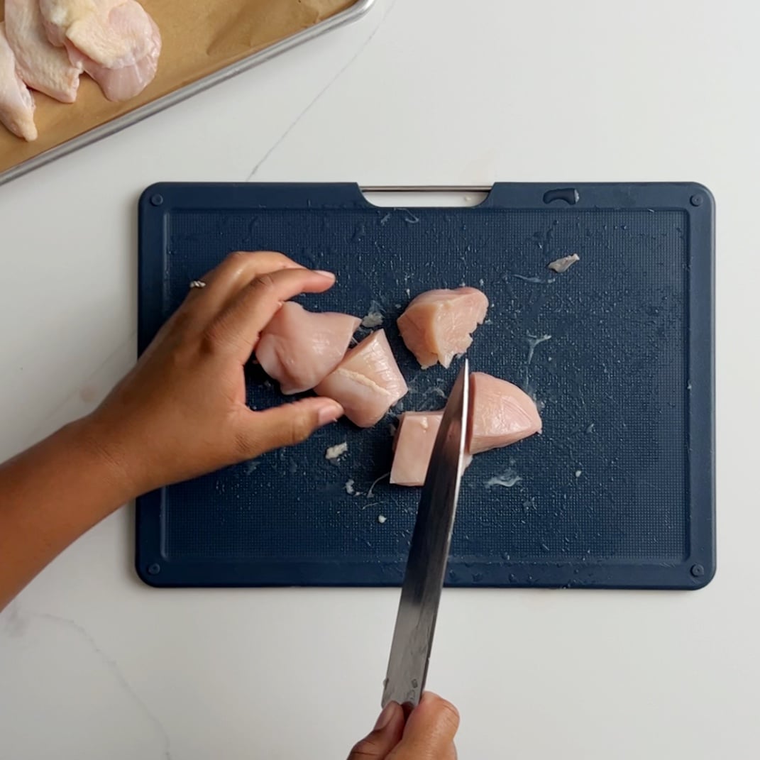 cutting chicken the breasts into 2 inch chunks on a blue cutting board