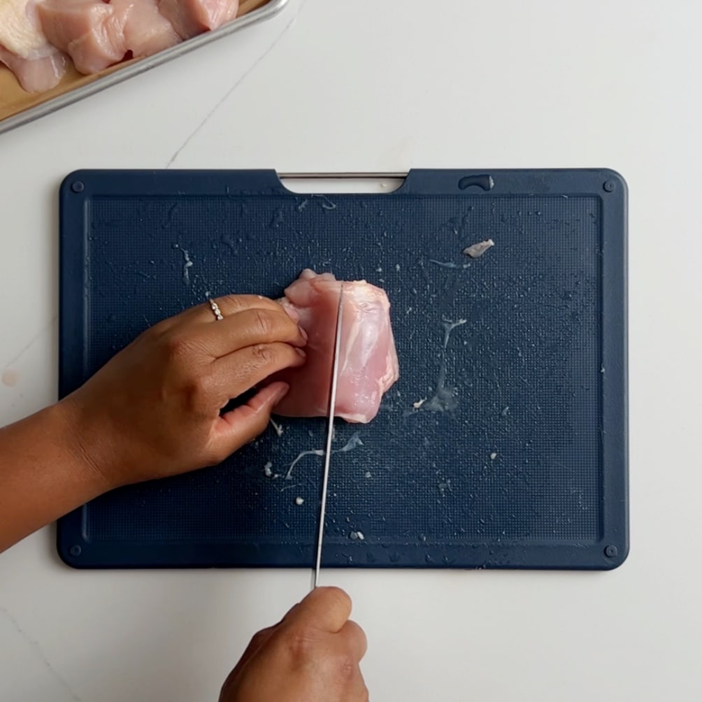 cutting the chicken thighs into halves on a blue cutting board