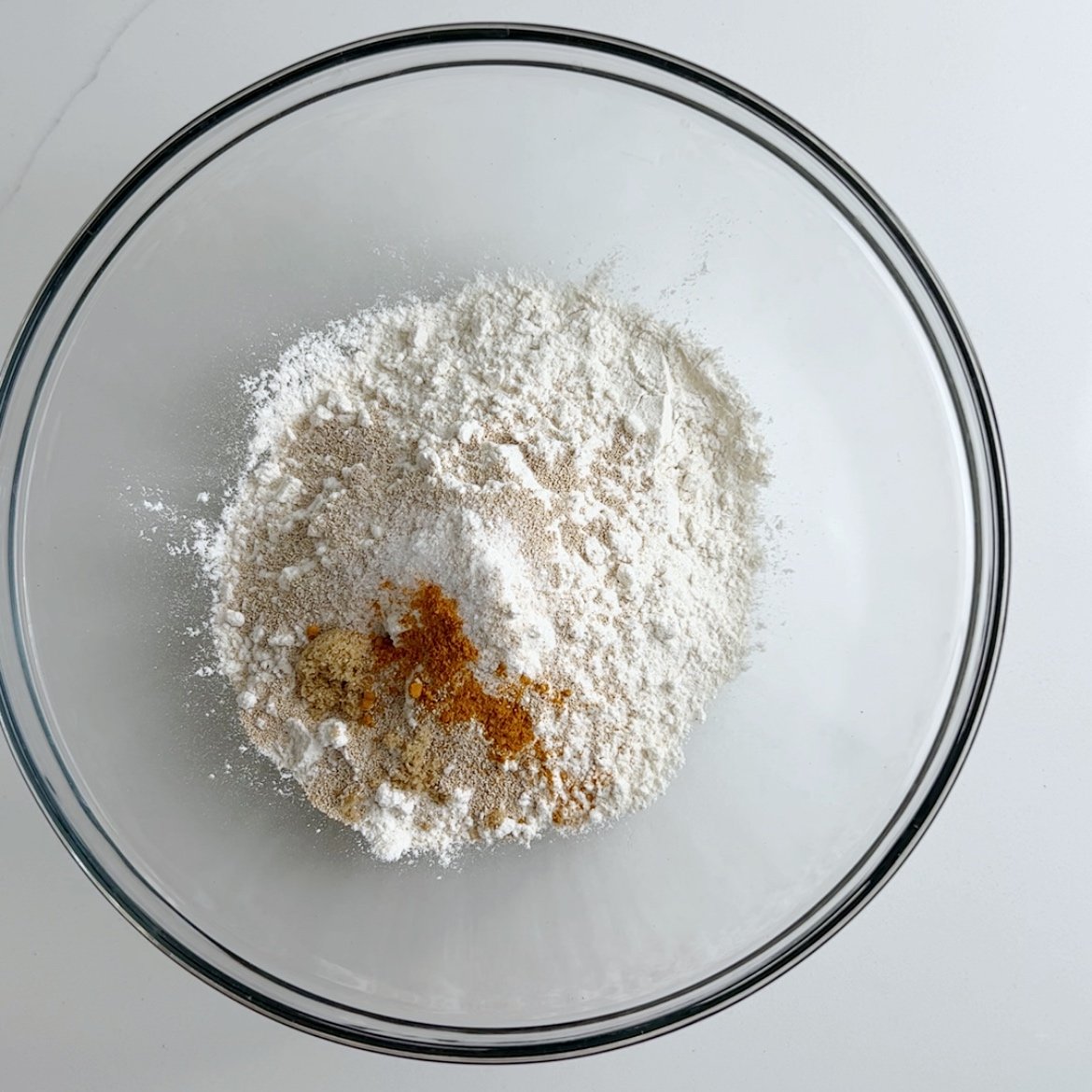 Gluten free flour, yeast, salt, sugar in a glass mixing bowl on a white marble surface