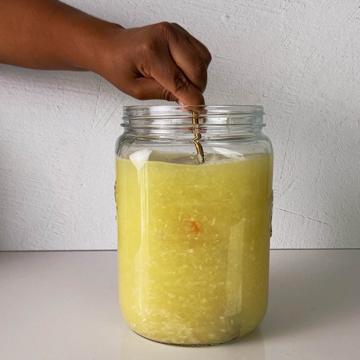 Brown hands stirring a mason jar filled to the top with grated ginger and water