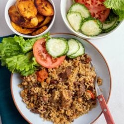 a bowl of Guyanese cook-up rice served with a side of fresh tomatoes, cucumbers, and lettuce and a bowl of plantains