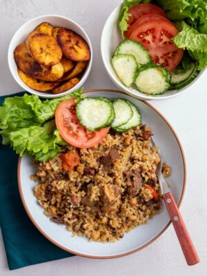 a bowl of Guyanese cook-up rice served with a side of fresh tomatoes, cucumbers, and lettuce and a bowl of plantains