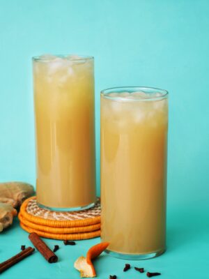 Two tall glasses of ginger beer on a teal back ground