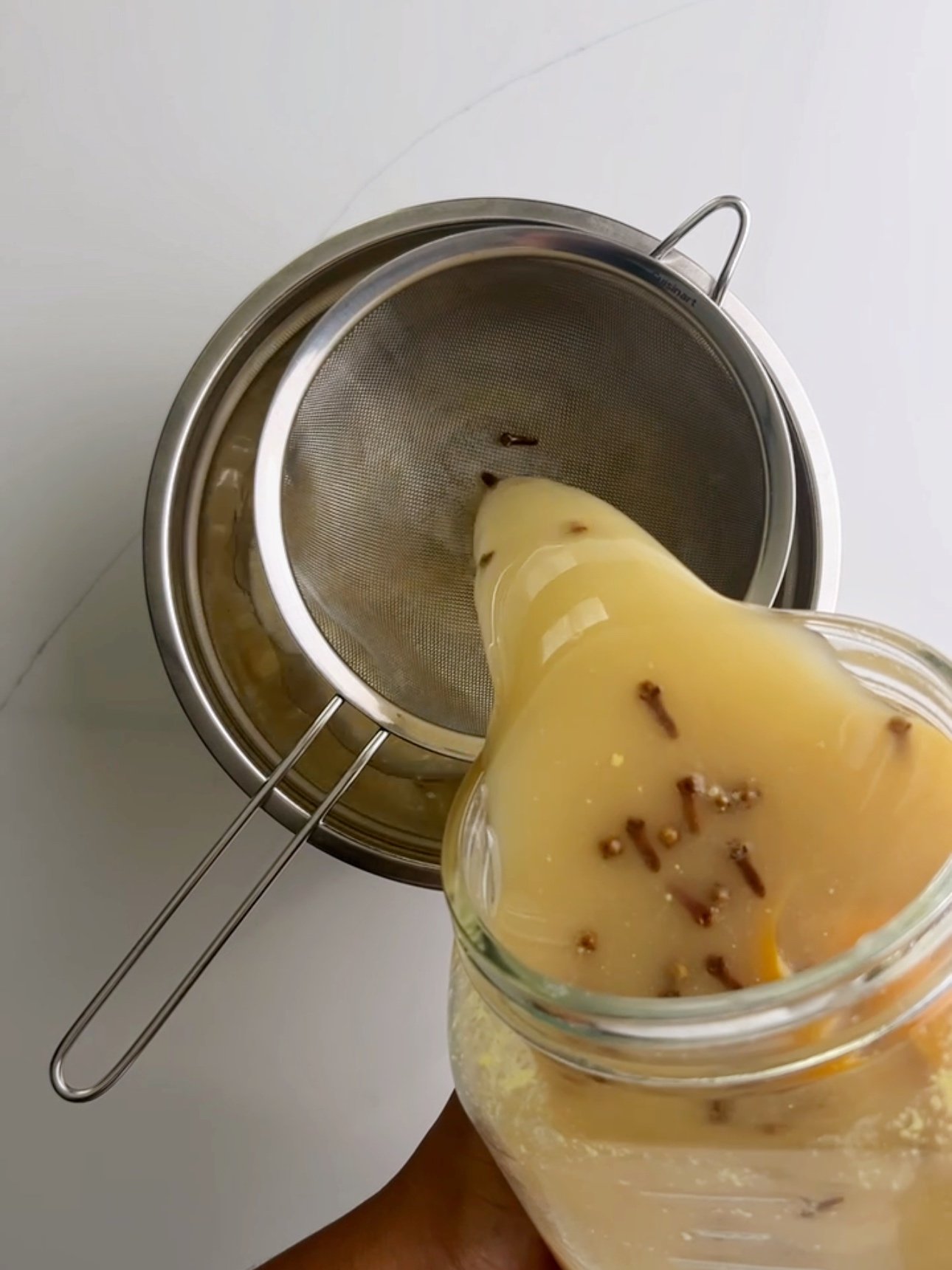 Pouring fermented ginger beer through a sieve and into a stainless steel bowl