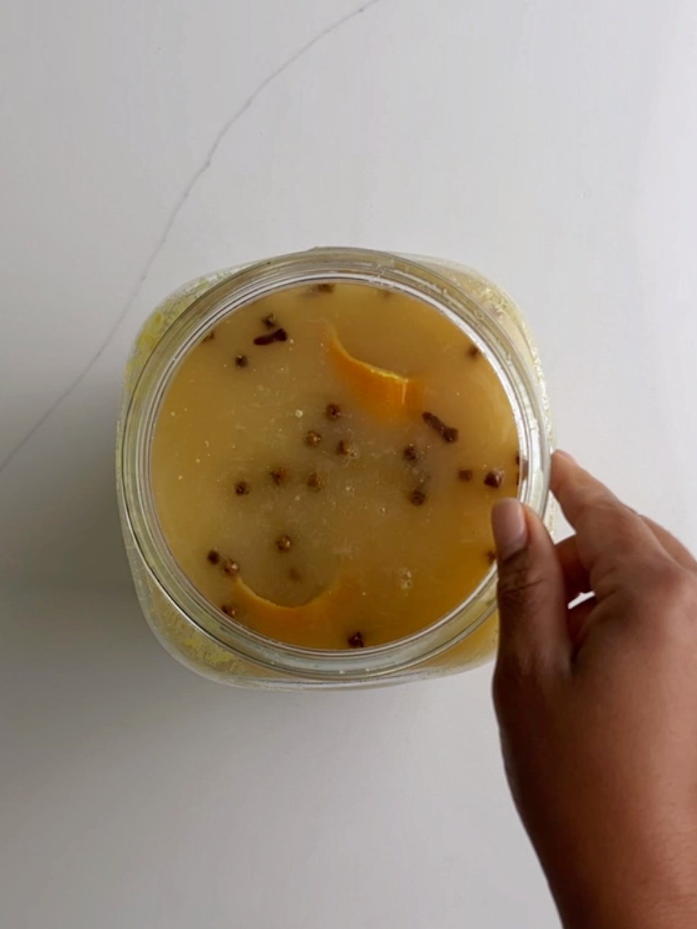 Fermented ginger beer in a glass jar with a hand to the right of the jar. 