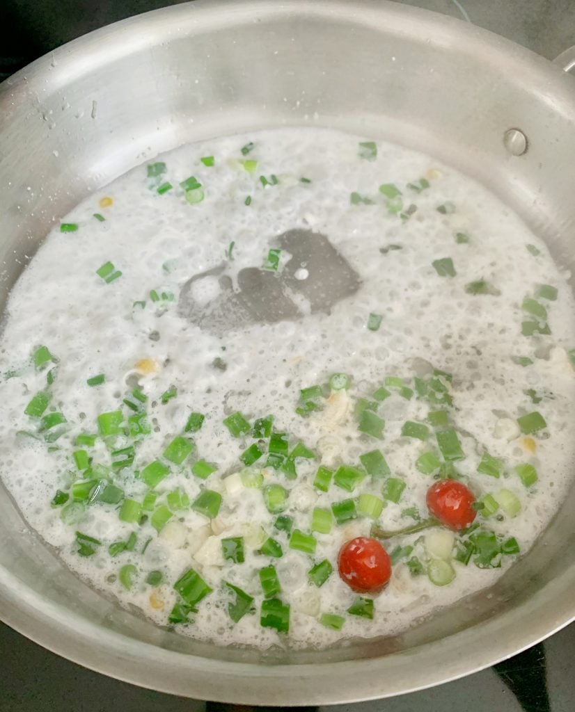 herbs and coconut milk cooking in a pot with wiri wiri peppers