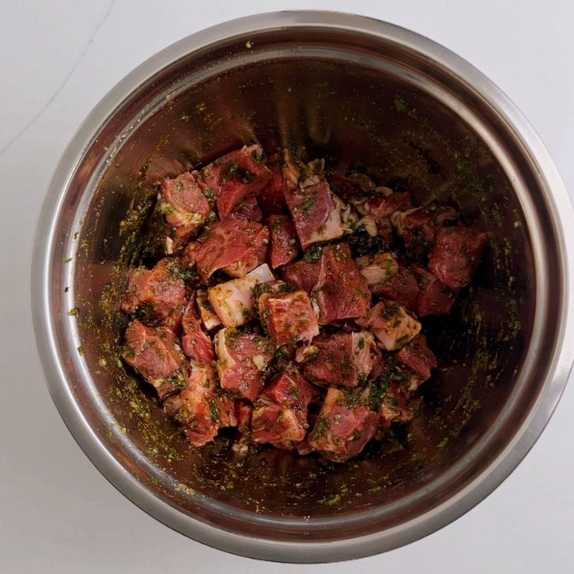 Cubed beef marinating in a large stainless steel bowl