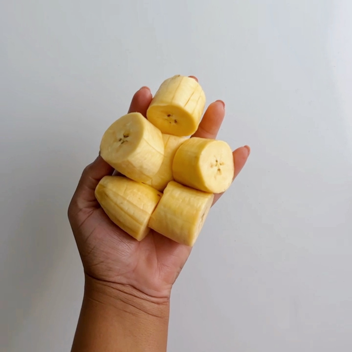 a hand holding peeled and diced plantains