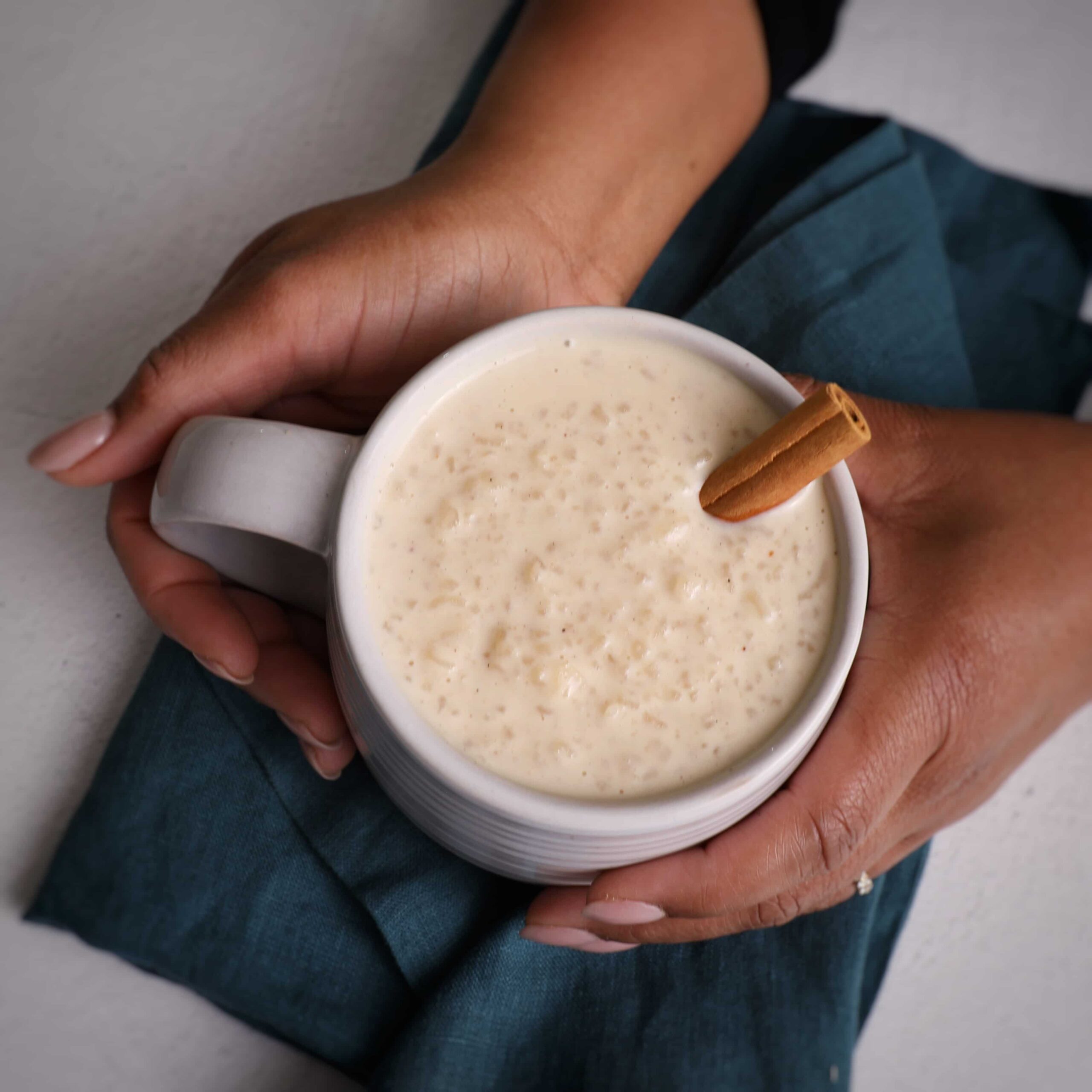 Hands holding a cup filled with porridge and a cinnamon stick sticking out of the top