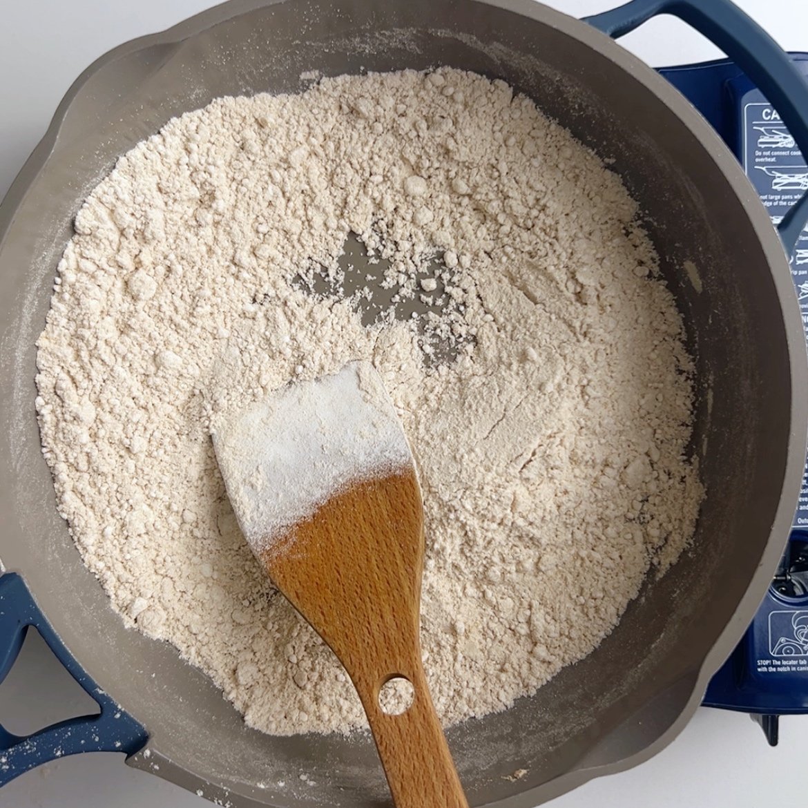 Flour in a gray frying pan with a wooden spoon. resting in the pan