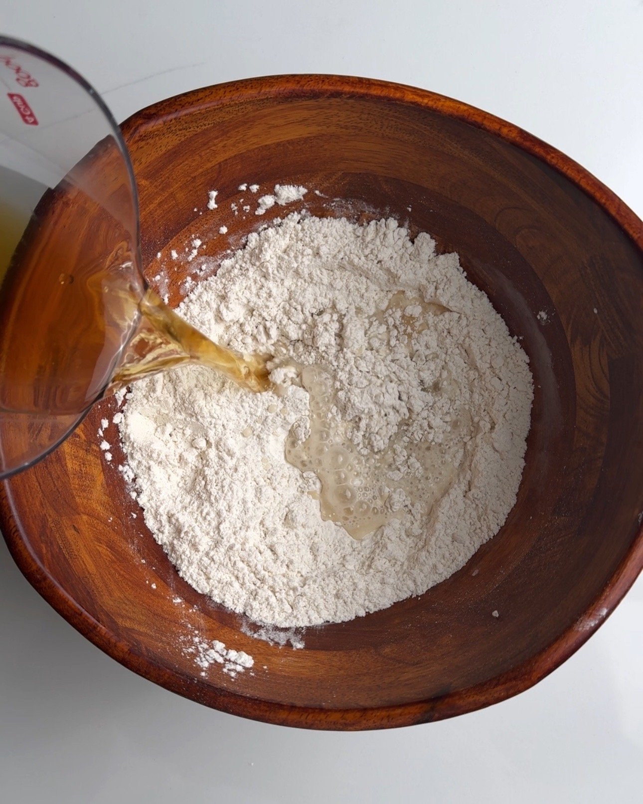 pouring water into a wooden bowl with flour