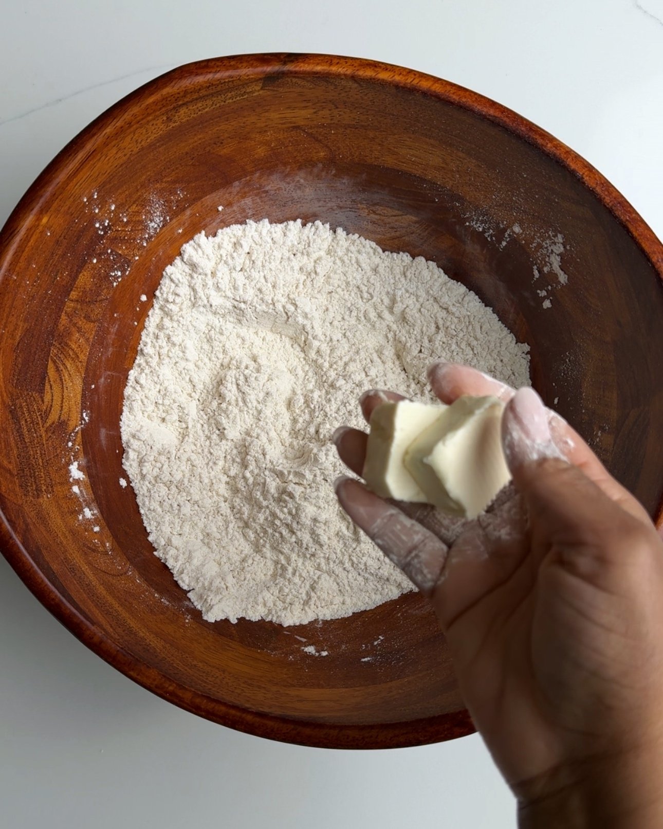 flour in a wooden bowl and butters in between finger tips
