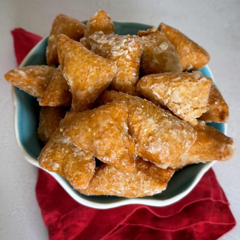 A blue bowl filled with golden brown mithai coated in sugar.