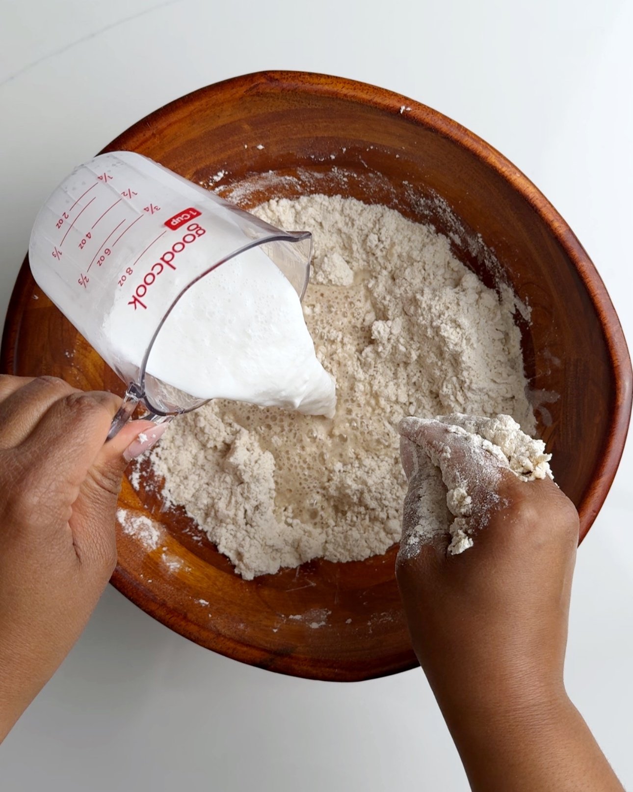 Pouring milk into a wooden bowl with flour 
