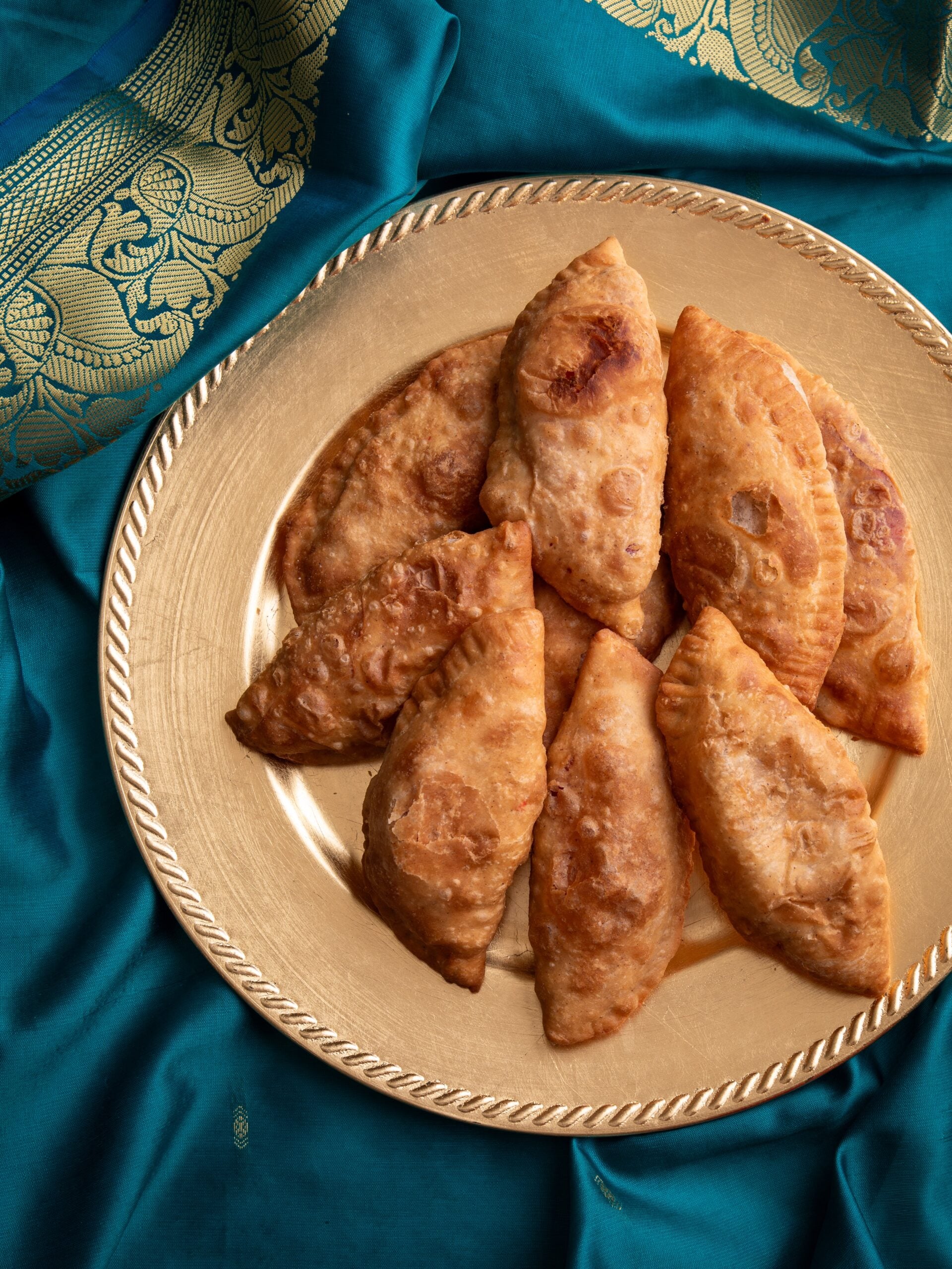 Gojas on a golden plate resting on a teal sari with a gold border.