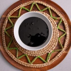 Guyanese cassareep poured out into a white bowl sitting on a woven coaster in a brown plate.