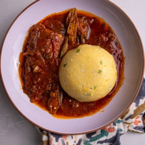 Close-up of coo coo and fish stew on a patterned napkin.