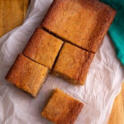 Overhead view of cassava pone squares arranged on parchment, with one piece pulled forward.