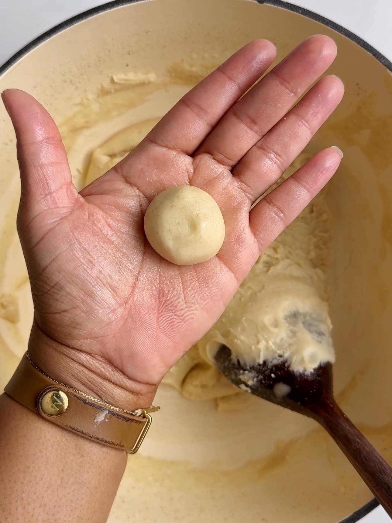 A hand holding a freshly shaped piece of peera dough above a pot with the cooked milk mixture in the background.
