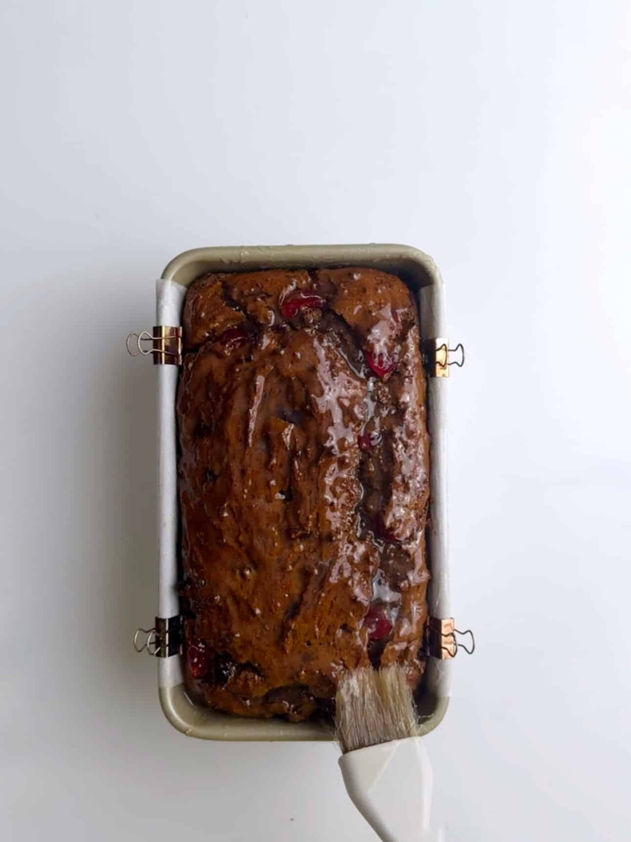 A baked Jamaican Easter bun in a loaf pan with a glossy glaze brushed over the top.