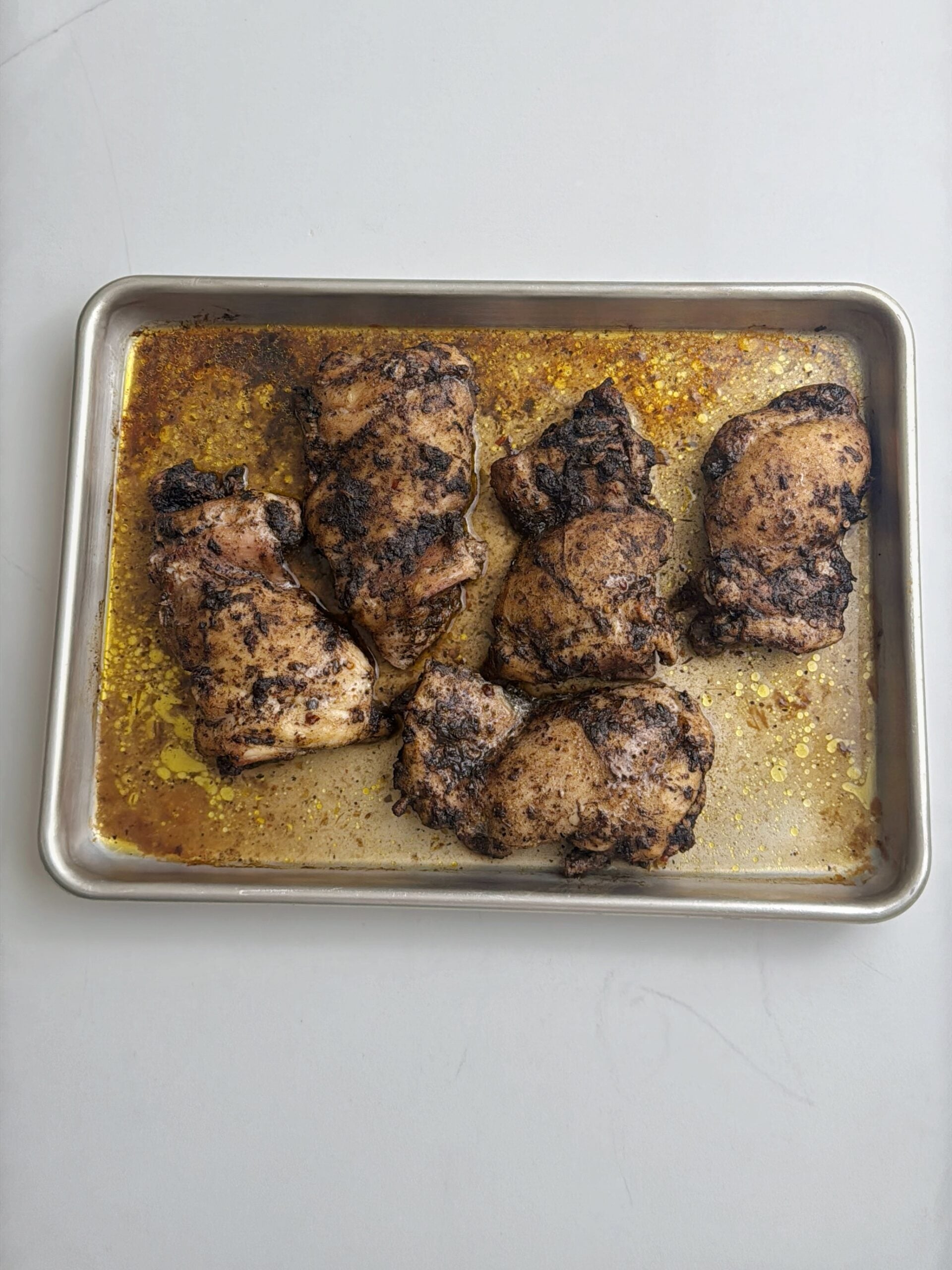 Roasted jerk chicken thighs resting on a baking sheet with pan drippings.