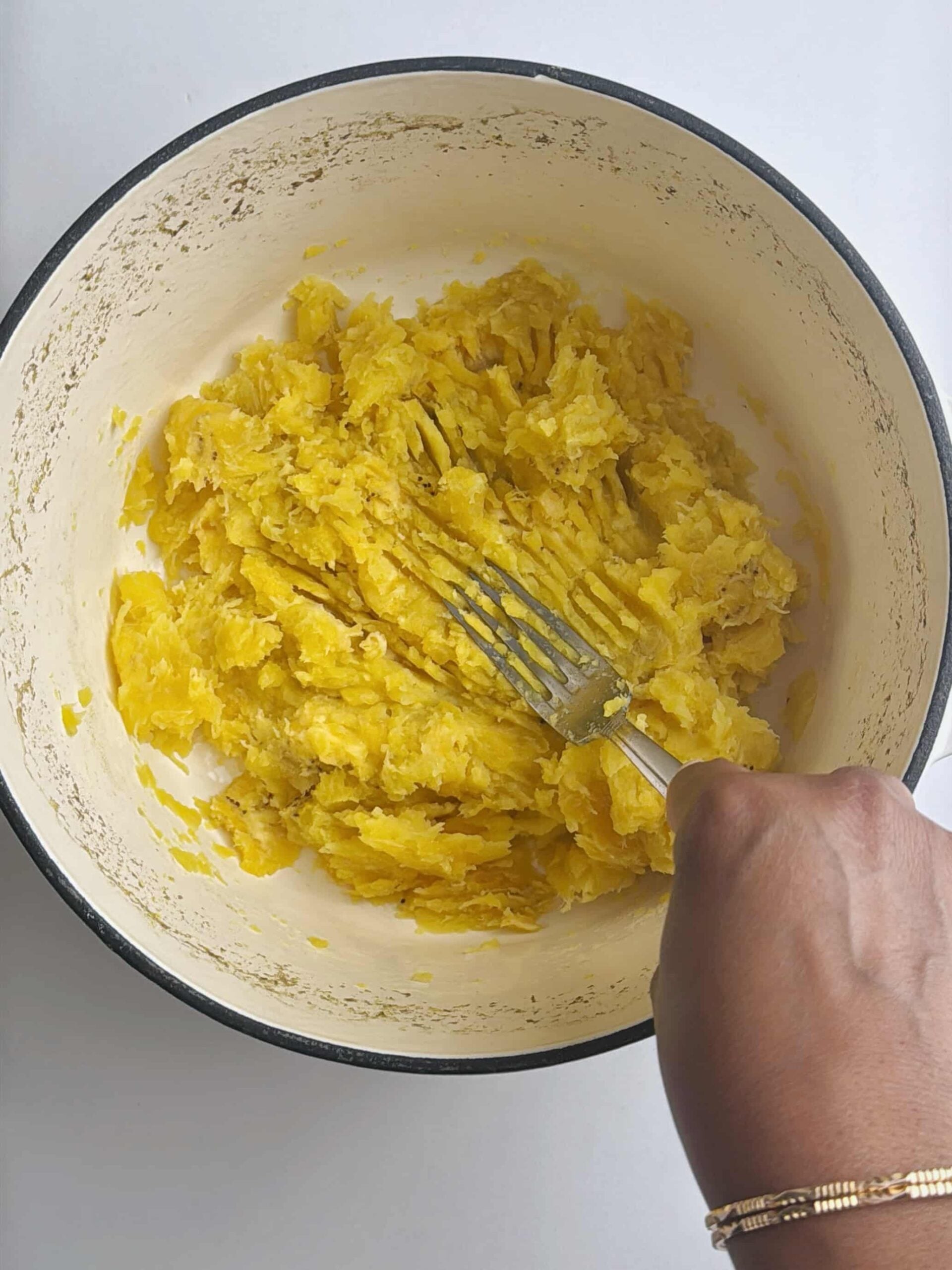 Cooked plantains being mashed in a bowl with a fork.