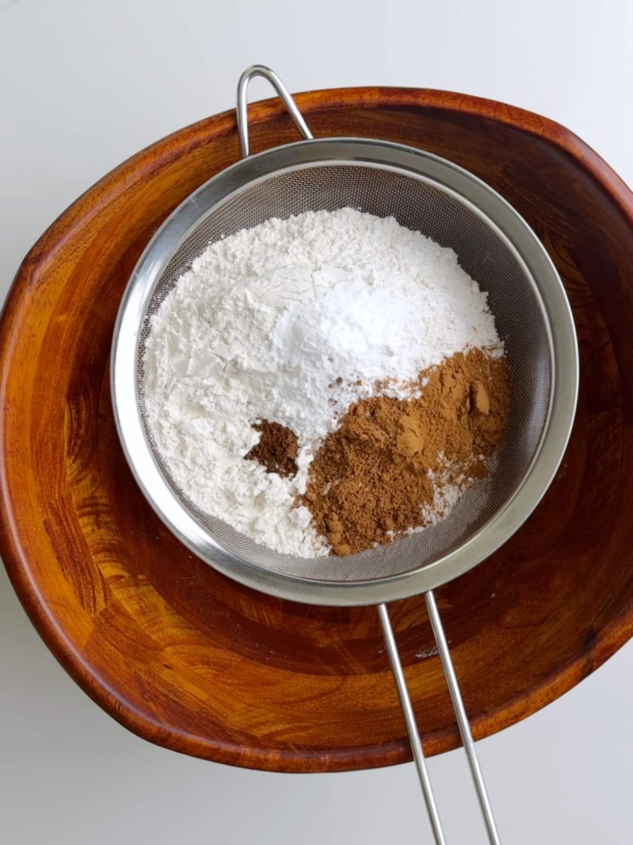 Dry ingredients including flour and spices being sifted together in a bowl.