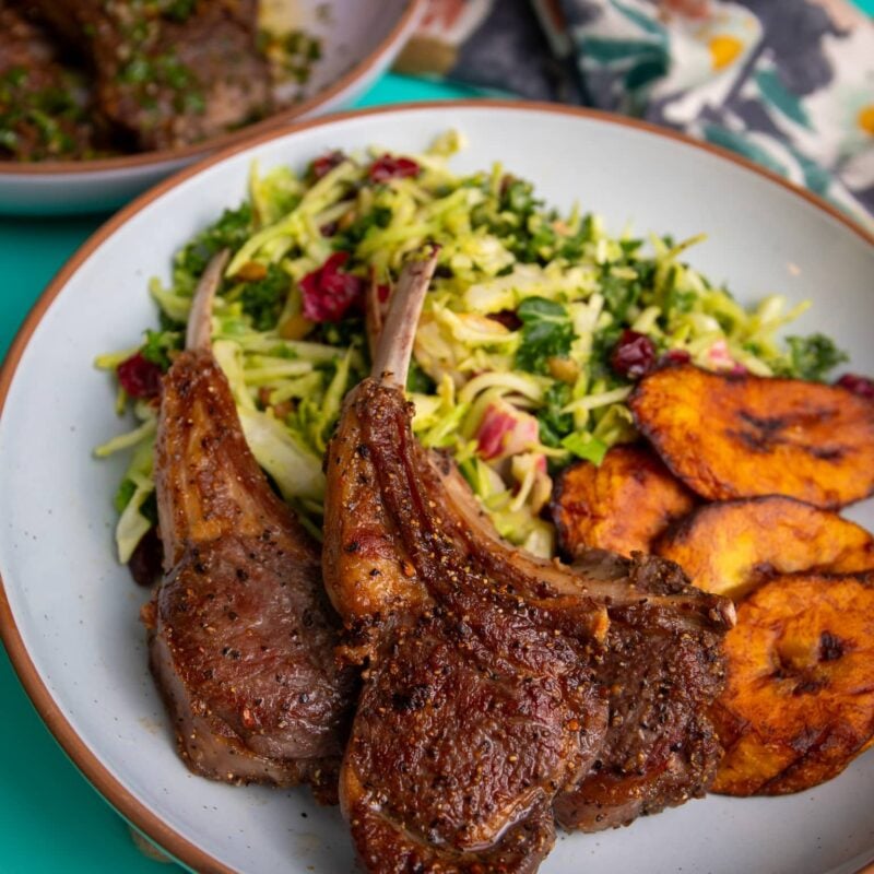 Plate of pan seared lamb chops served with fresh salad and fried plantains.