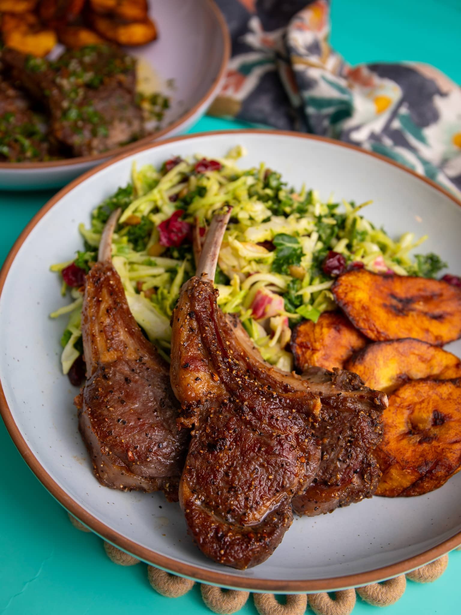 Plate of pan seared lamb chops served with fresh salad and fried plantains.