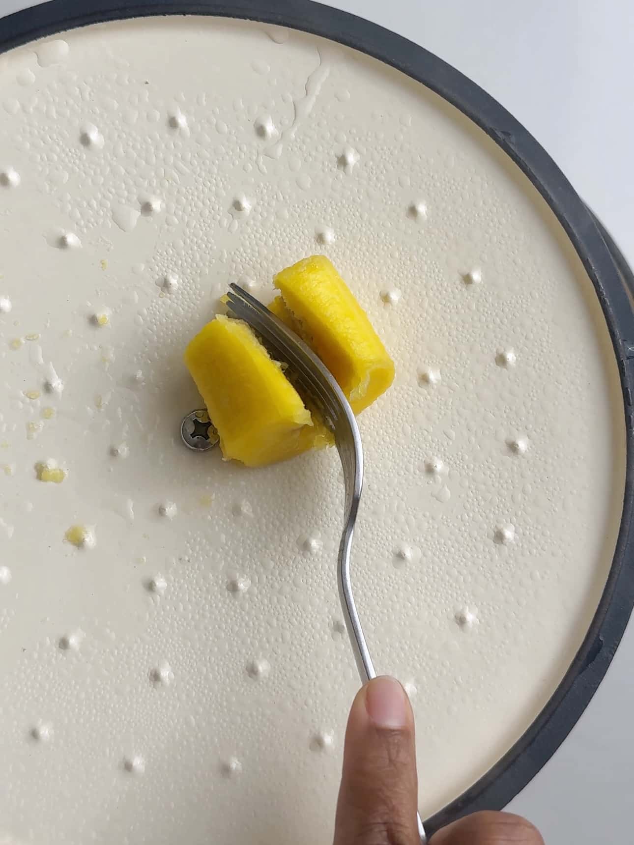 Fork testing the softness of a cooked plantain piece.