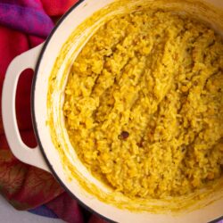 Cooked Guyanese kitchri with rice and split peas in a Dutch oven on a colorful cloth.