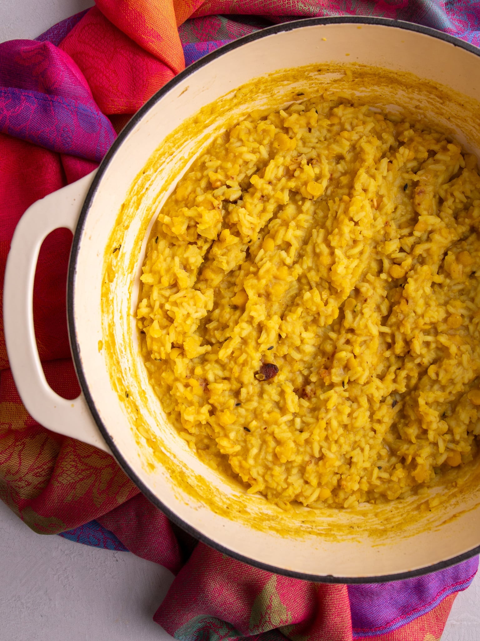 Cooked Guyanese kitchri with rice and split peas in a Dutch oven on a colorful cloth.