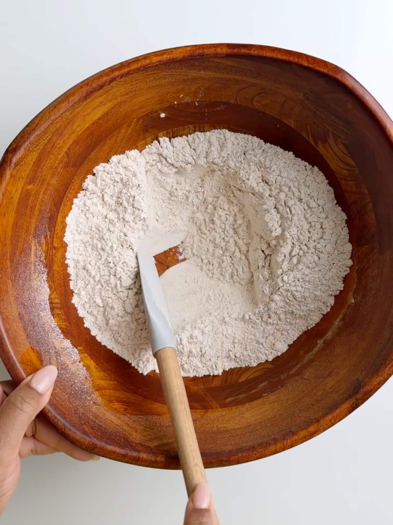 Gluten free flour mixture being combined in a wooden bowl with a spatula.