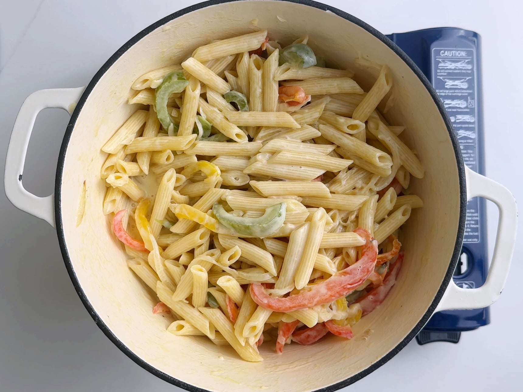 Penne pasta tossed with creamy sauce and peppers in a large pot.
