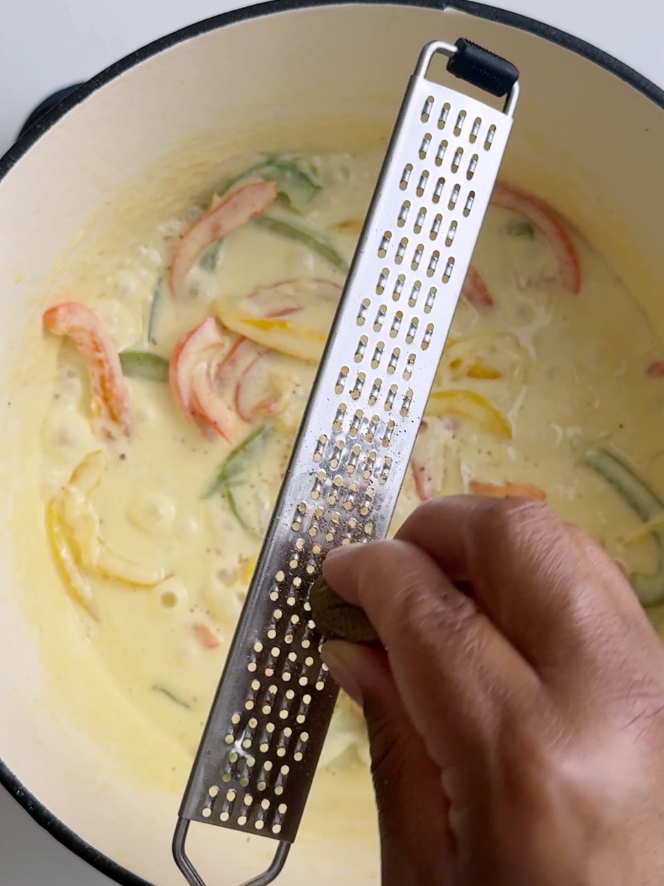 Fresh nutmeg being grated into the creamy jerk pasta sauce.